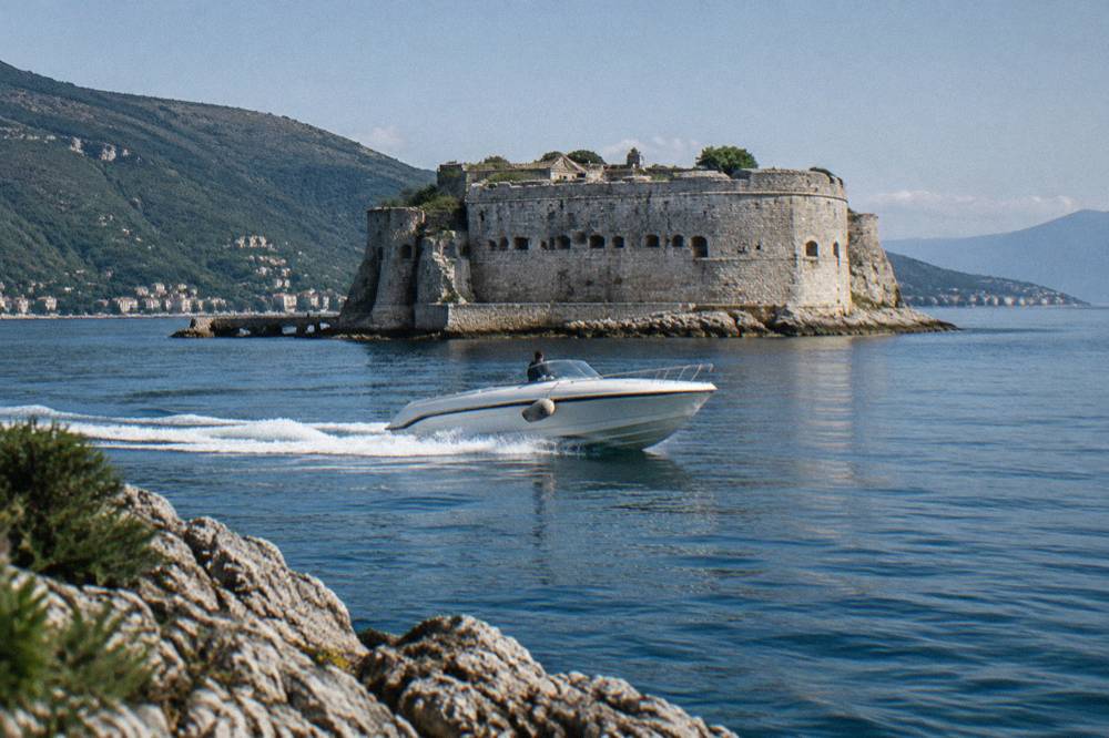 Speedboat on calm blue water passing a fortified island near a coastal town