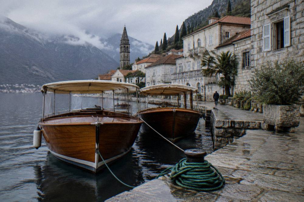 Small wooden tour boats moored at a stone quay beside a waterfront of old stone buildings