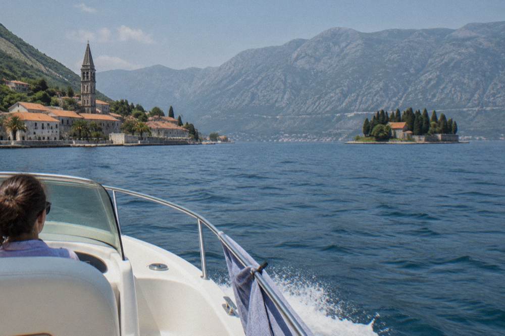 A speedboat crossing open bay water toward islands and mountains under a clear sky