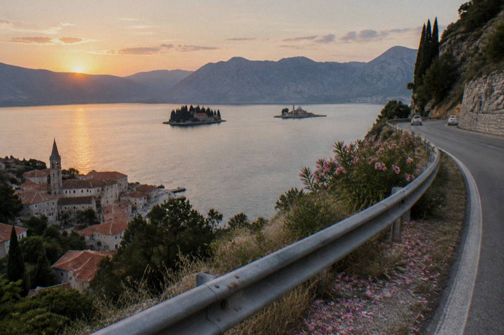 A coastal road curving along a bay with a stone town and islands in the distance