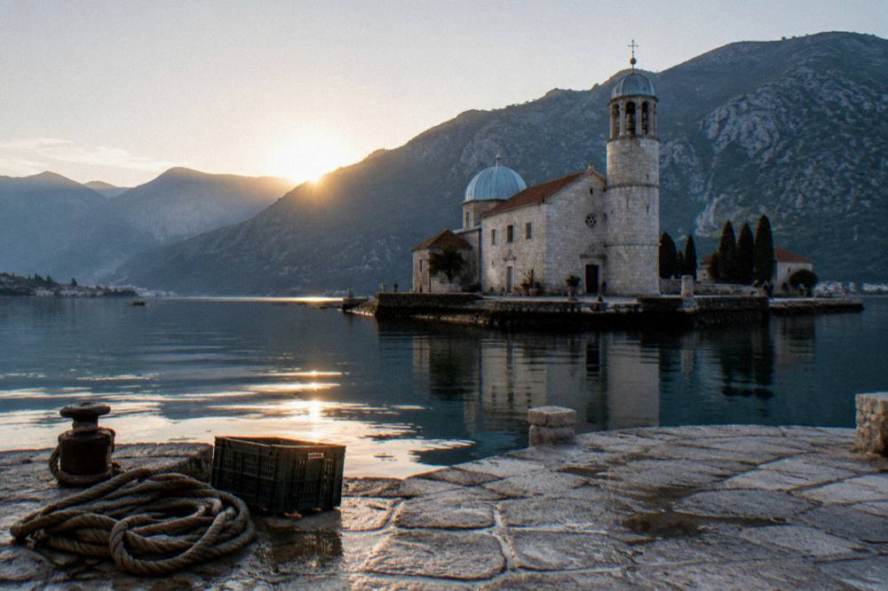 Morning light over a calm bay with a fortified island church and mountains behind