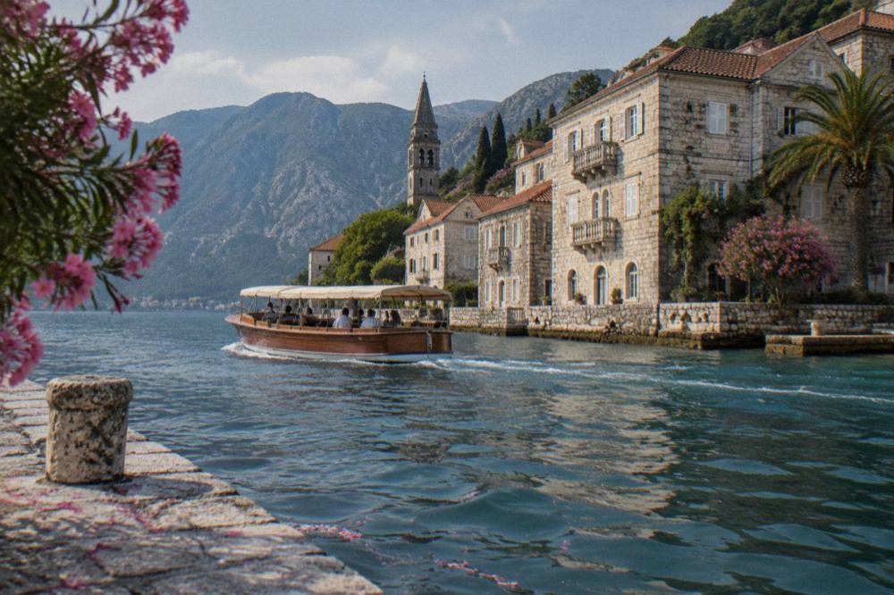 A wooden speedboat with an awning cruising past stone buildings at the waterline in Perast
