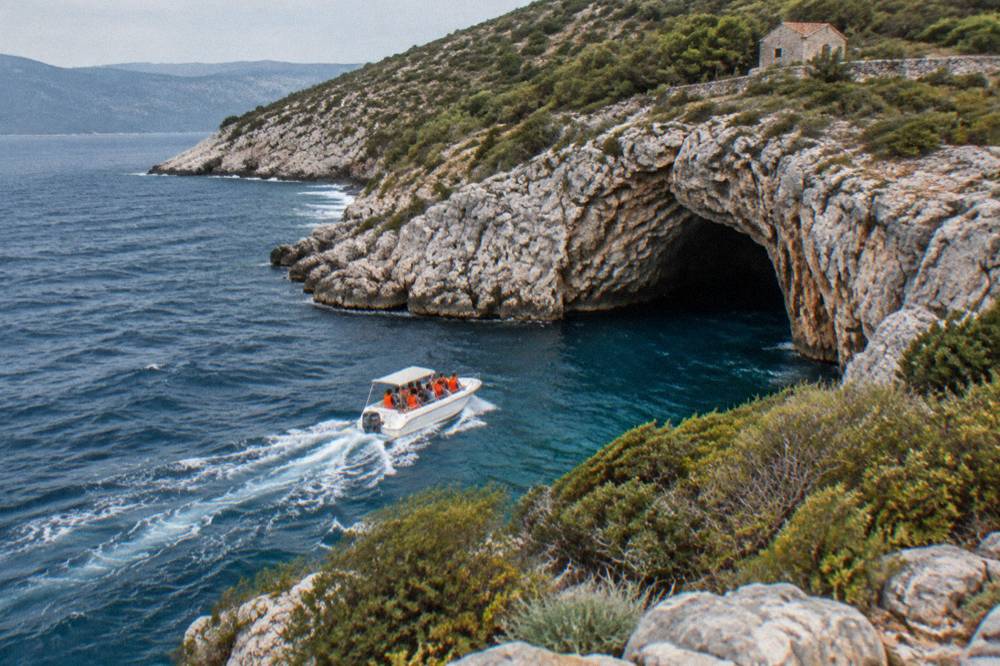 A speedboat with passengers in life vests entering a rocky bay toward a cave opening