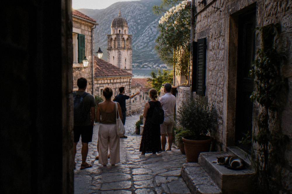 A guide speaking to a small group beside the stone walls and narrow lane of an old Mediterranean town