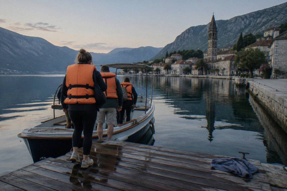 Travellers in life vests boarding a small boat at a wooden jetty on a calm morning