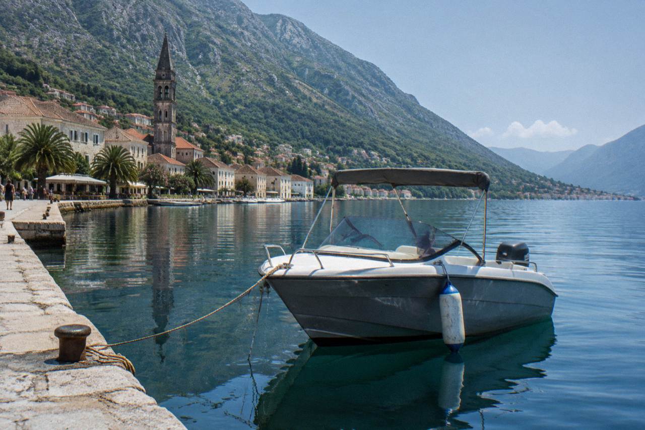 A small speedboat moored on calm blue water below steep green hills on the Bay of Kotor