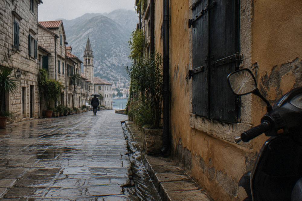 A narrow stone street in Kotor Old Town lined with shuttered buildings and a parked scooter