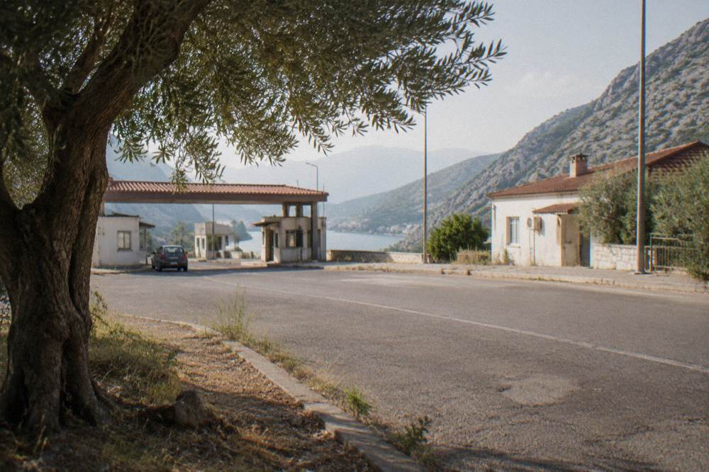 A quiet border checkpoint road with low buildings and hills on both sides