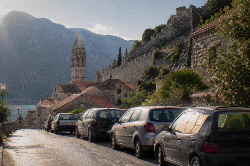 A stone fortification wall rising above red rooftops and parked cars in an old coastal town
