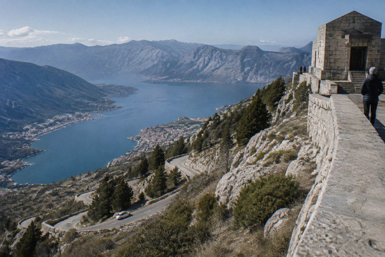 A winding coastal road above the blue water of the Bay of Kotor with hillsides rising steeply