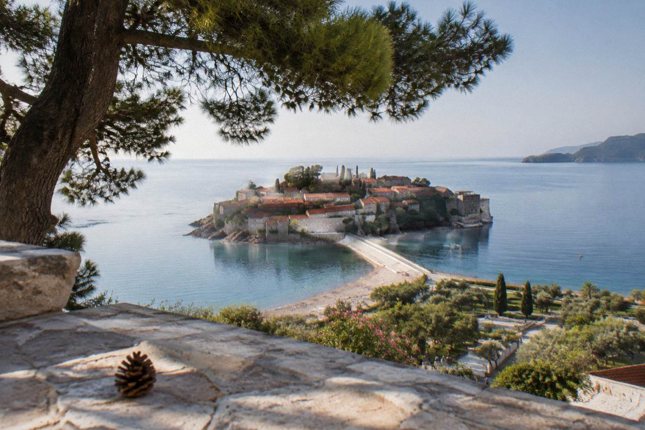 The islet of Sveti Stefan connected to the mainland by a narrow causeway above pine trees and clear sea
