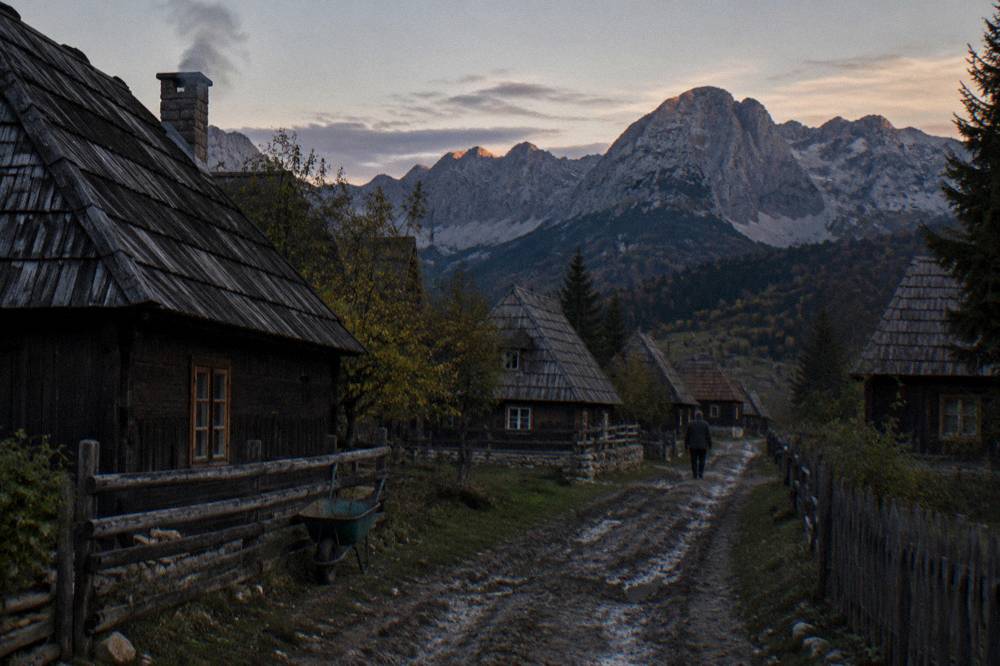 A small mountain town of wooden houses beneath grey peaks at dusk