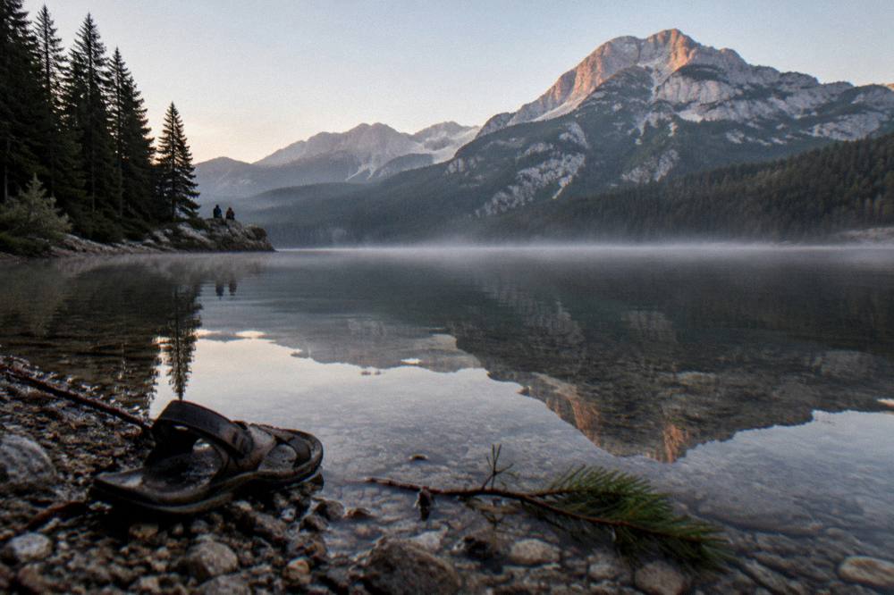 A calm dark mountain lake ringed by pine forest and high peaks