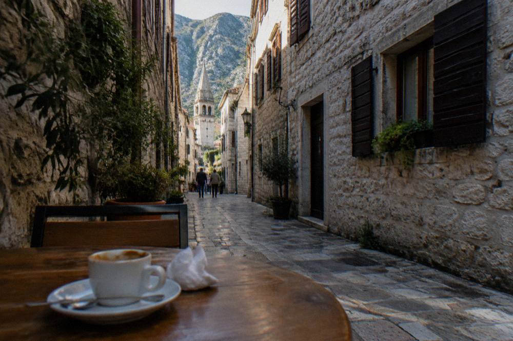 Narrow stone lane in Kotor Old Town with shuttered buildings and a cafe table