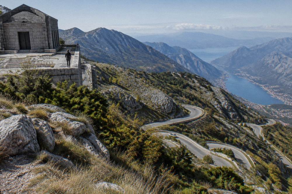 Winding mountain road with hairpin bends descending toward a bay below