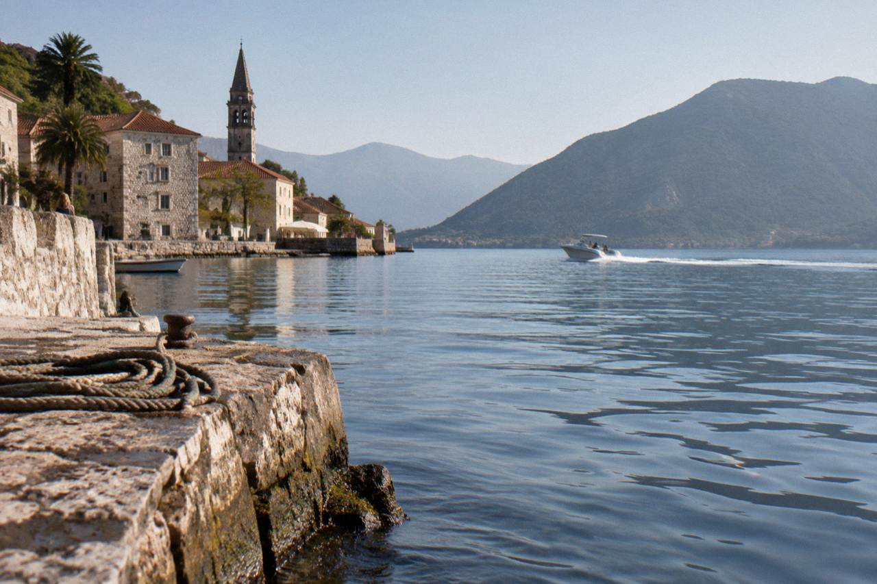 Speedboat crossing calm blue water in the Bay of Kotor toward wooded hills