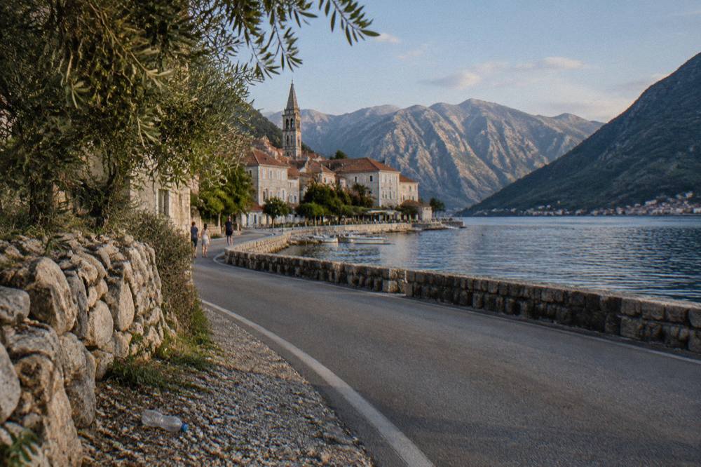 Coastal road curving along a blue bay with steep mountains rising on both sides