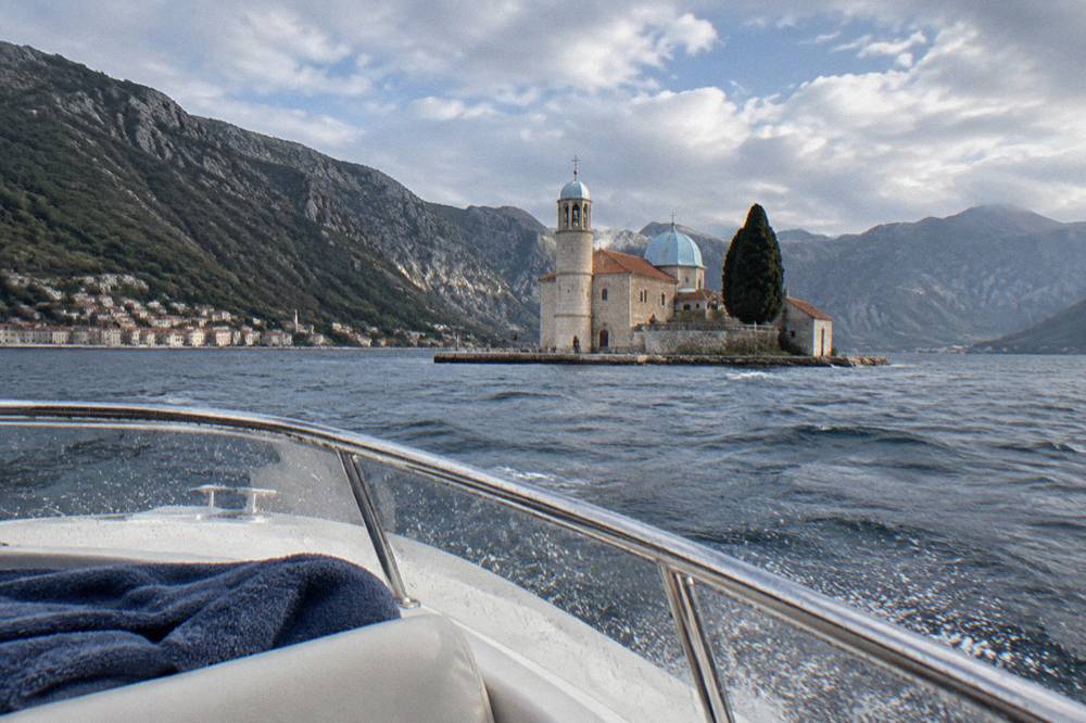 Speedboat crossing open water toward a rocky island with a stone church on it
