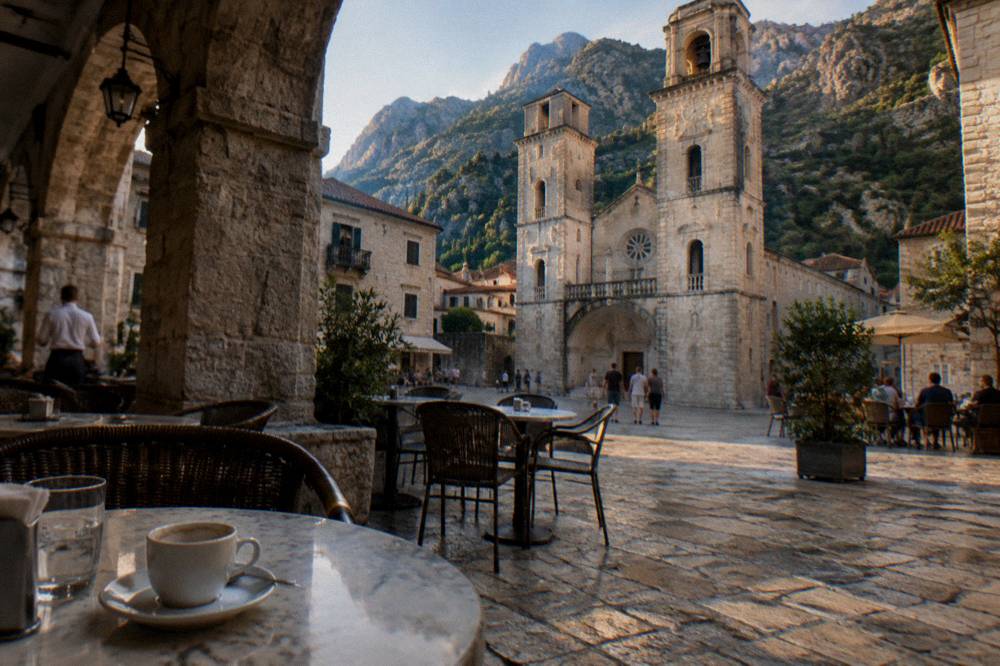Stone old town square with cafe tables and a church tower in late afternoon light