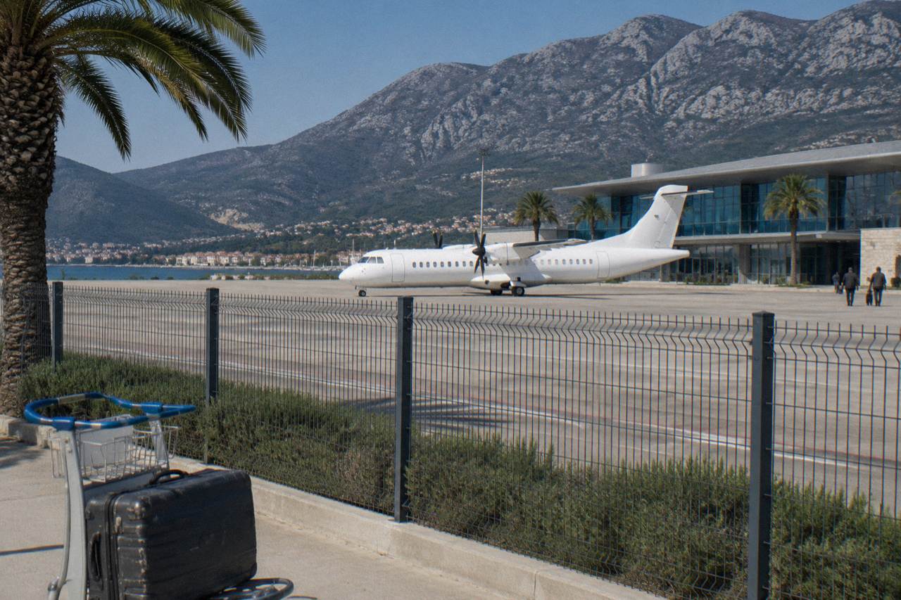 Small airport terminal building beside a runway with hills rising behind it under a clear sky
