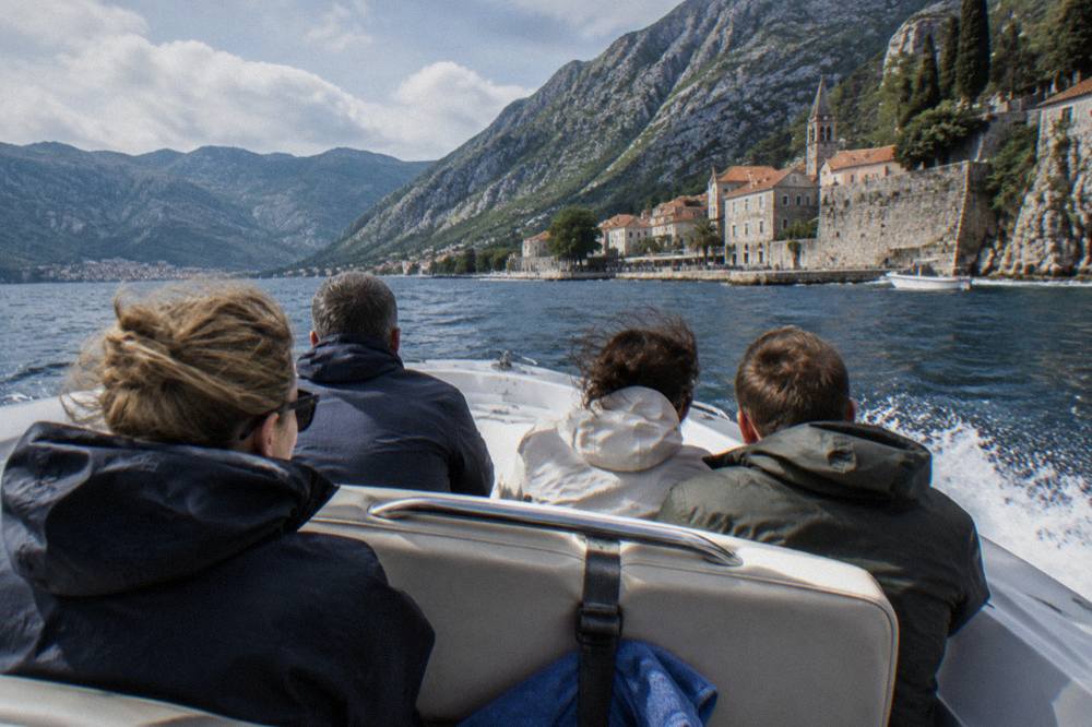 Speedboat passengers in windbreakers and sunglasses heading across the blue water of the Bay of Kotor