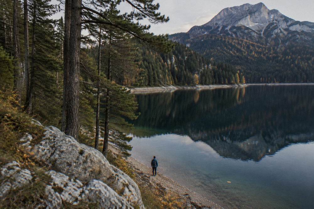 Hiker in a fleece and windbreaker beside the dark water of Black Lake below pine forest