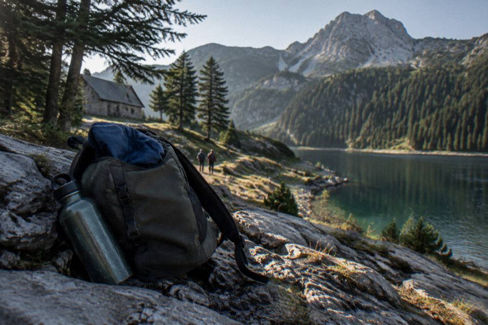 Small daypack with water bottle and folded jacket resting on a stone wall above a mountain lake