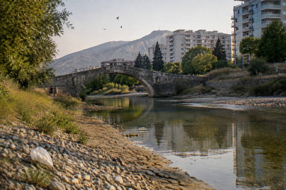 Stone bridge over a river in Podgorica with modern buildings behind it